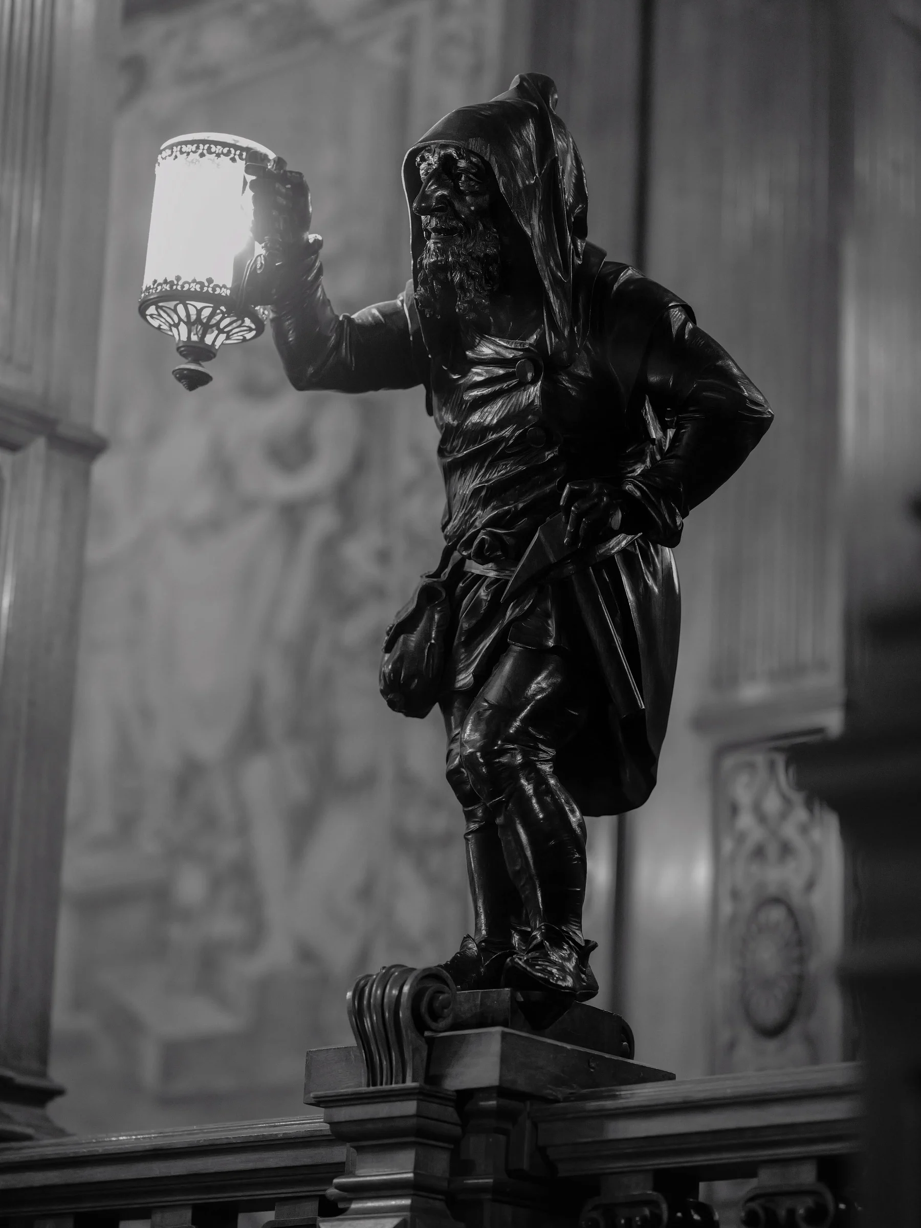 Black and white image of a statue holding a lantern inside Peleș Castle